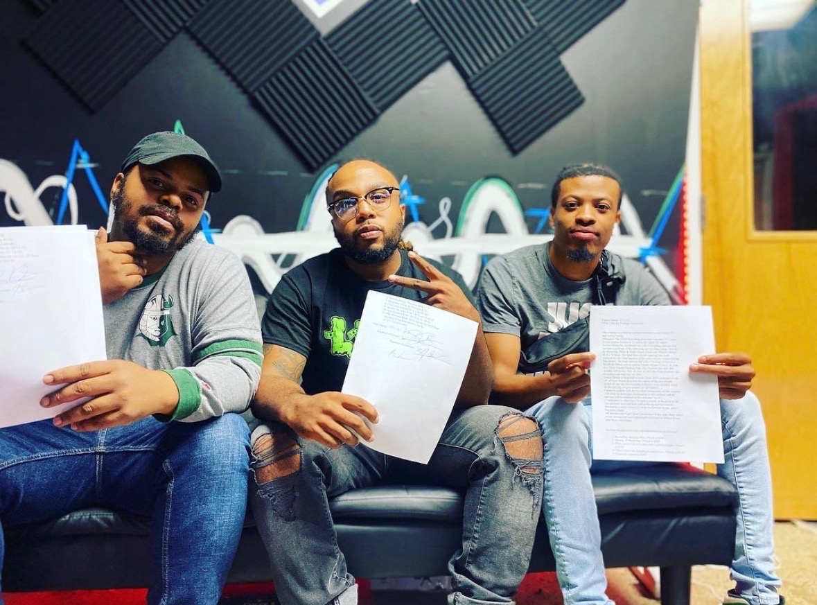 Three team members holding signed Luxary Group Co. agreements in the studio